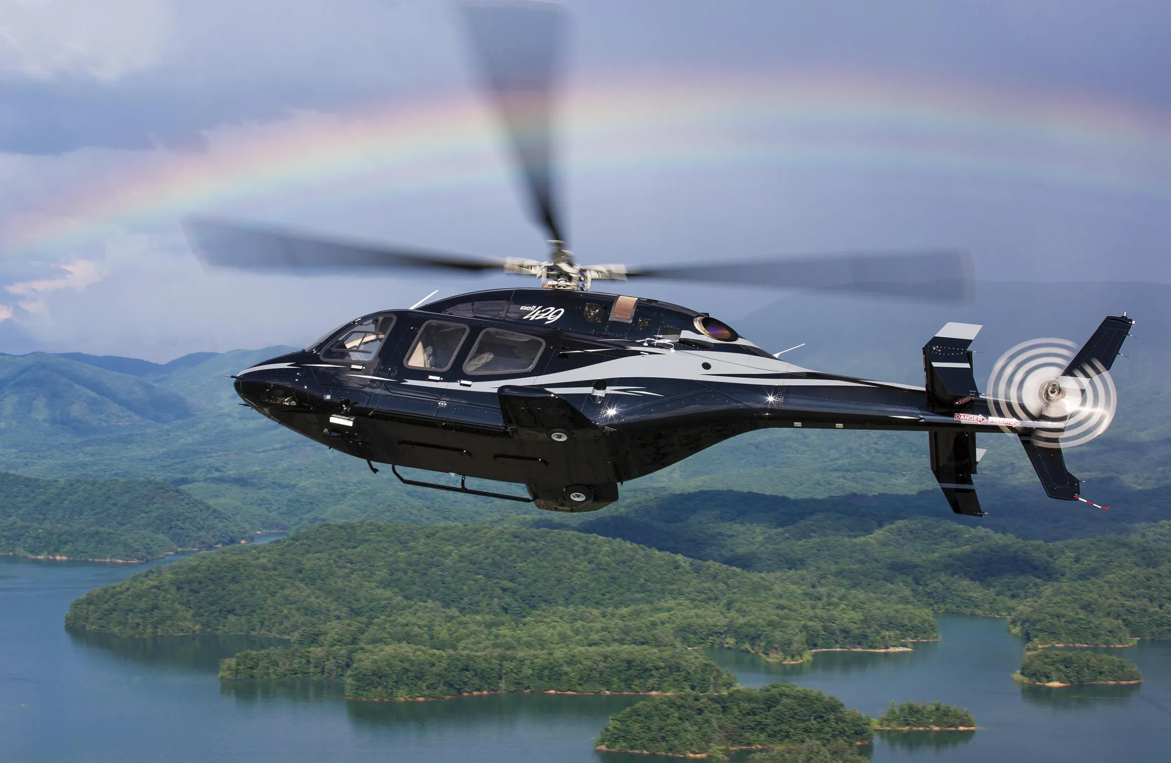 A black helicopter flying over wooded lakes