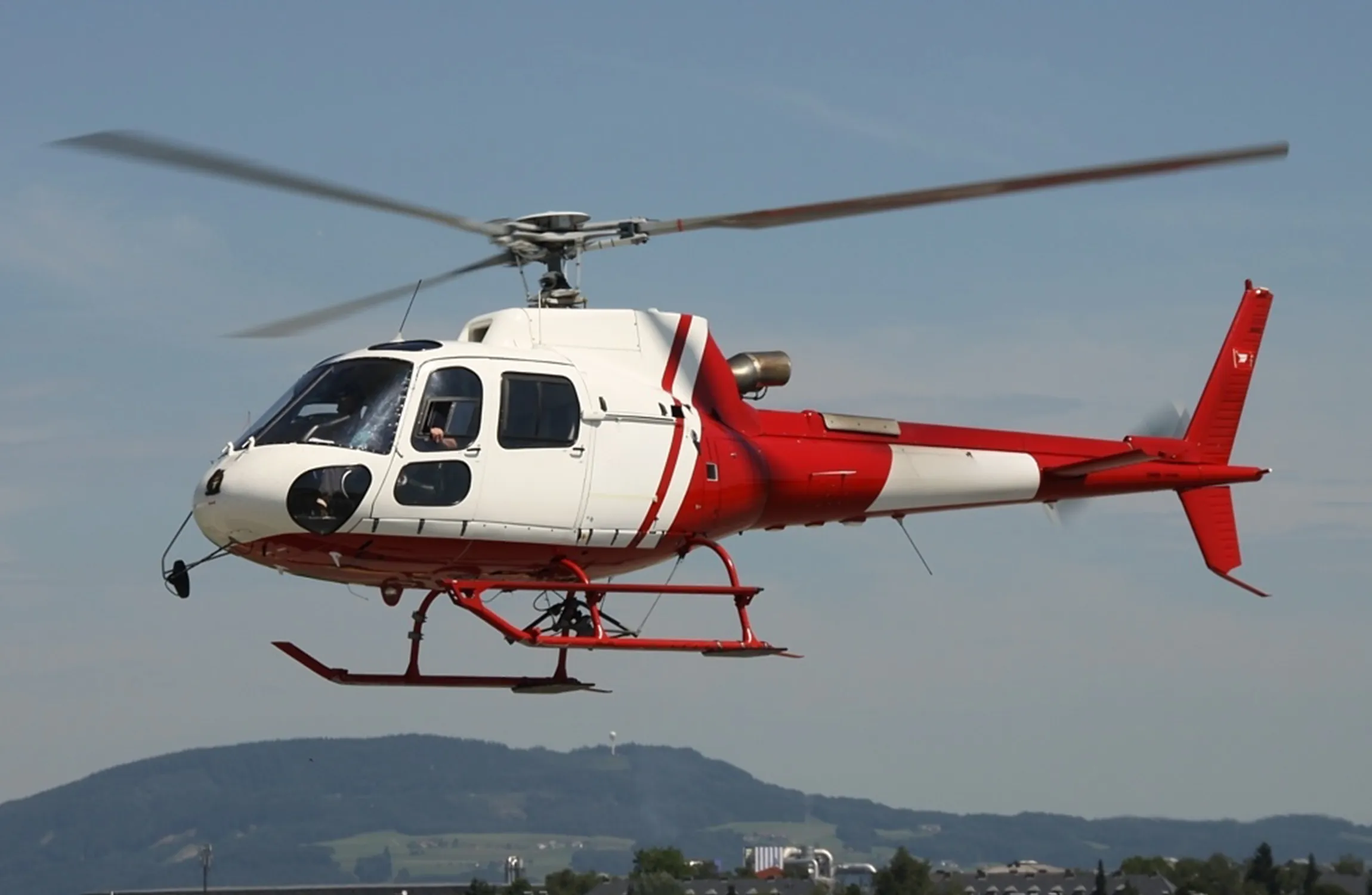 A white and red helicopter flying above an urban area