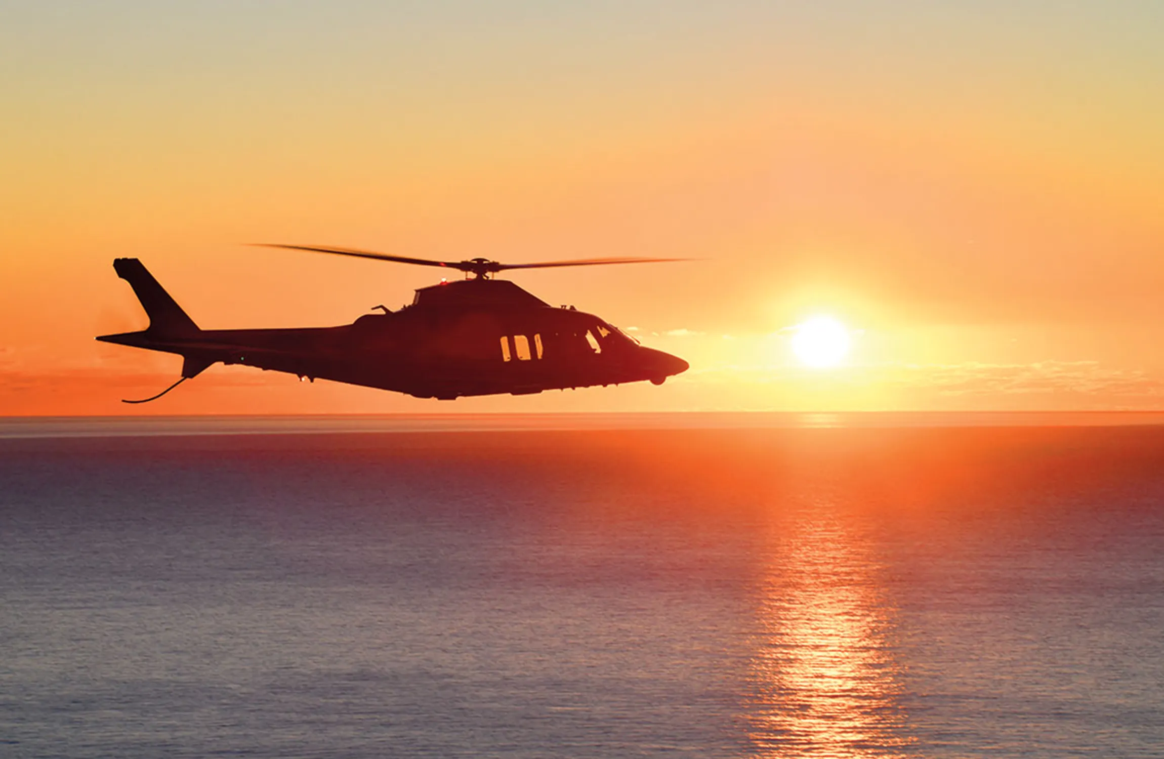 A helicopter flying over water at sunset
