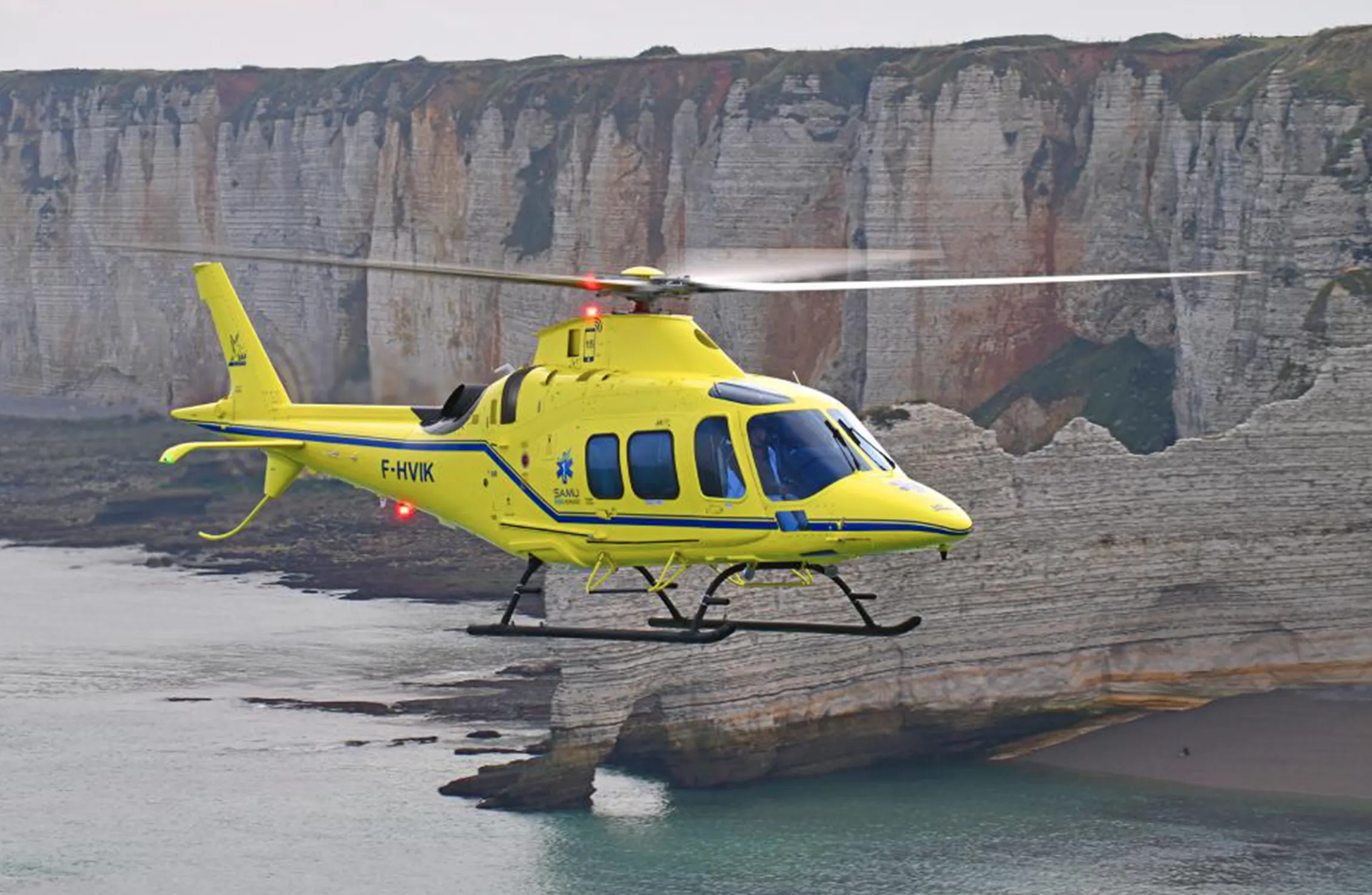 A yellow helicopter flying along cliffs