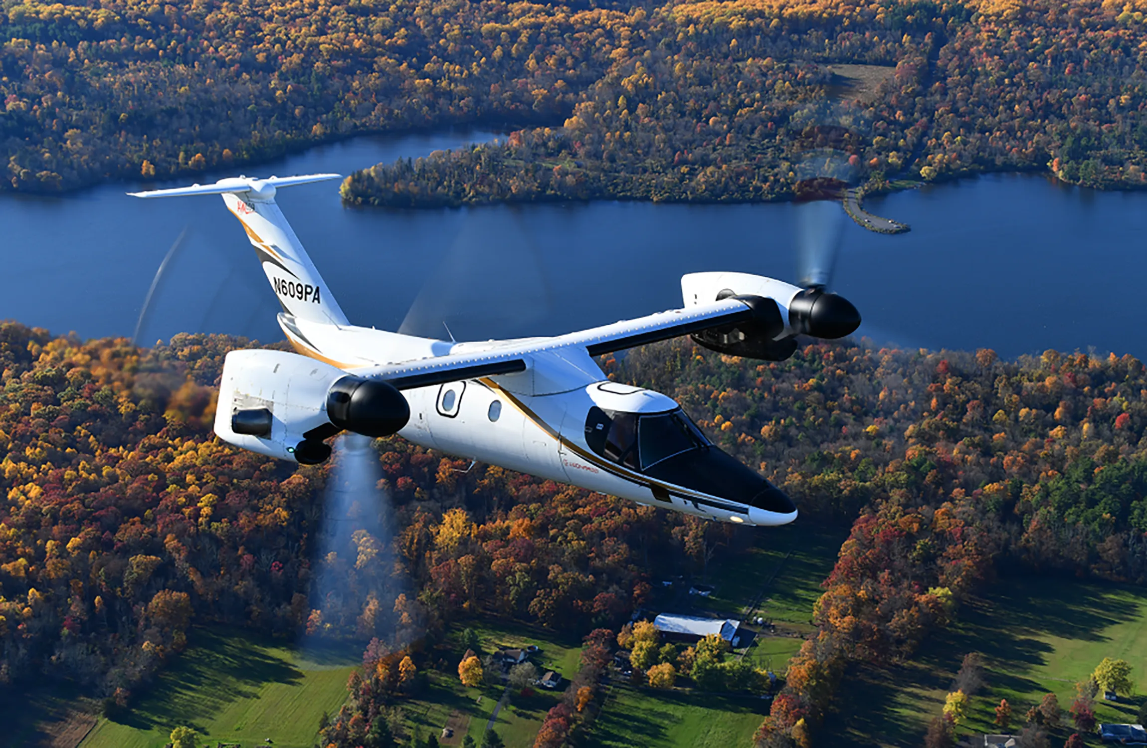 A twin prop helicopter flying over a wooded lake