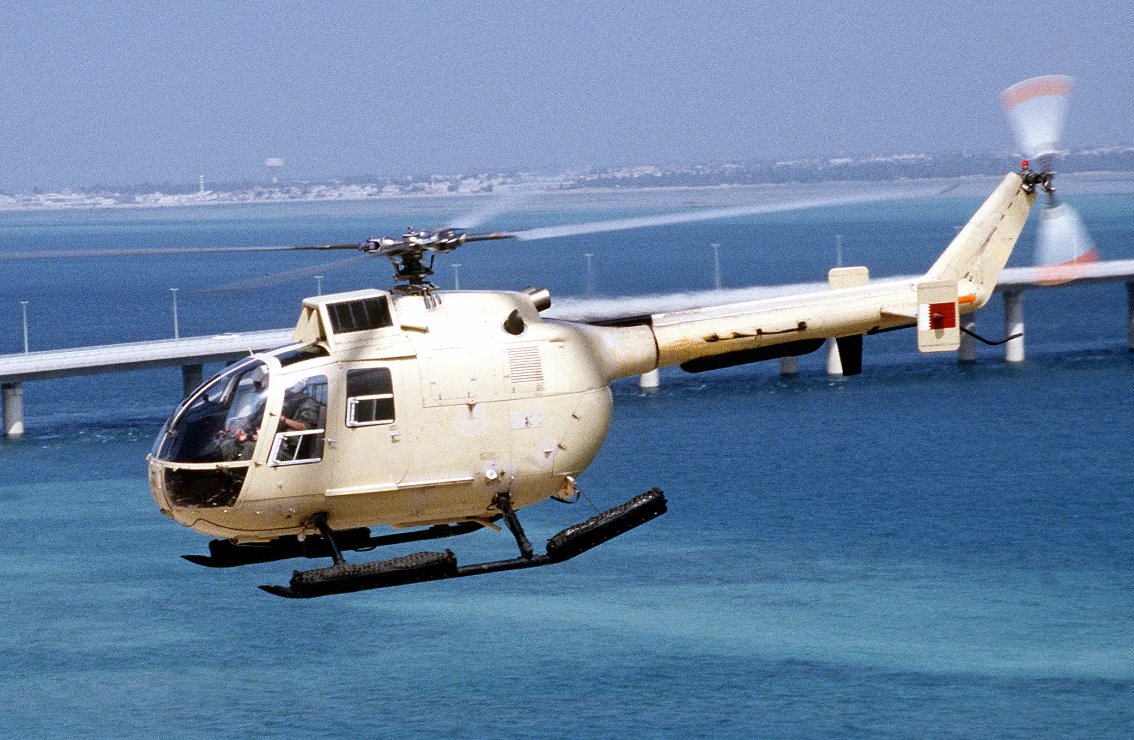 A white helicopter flying over water in an urban area