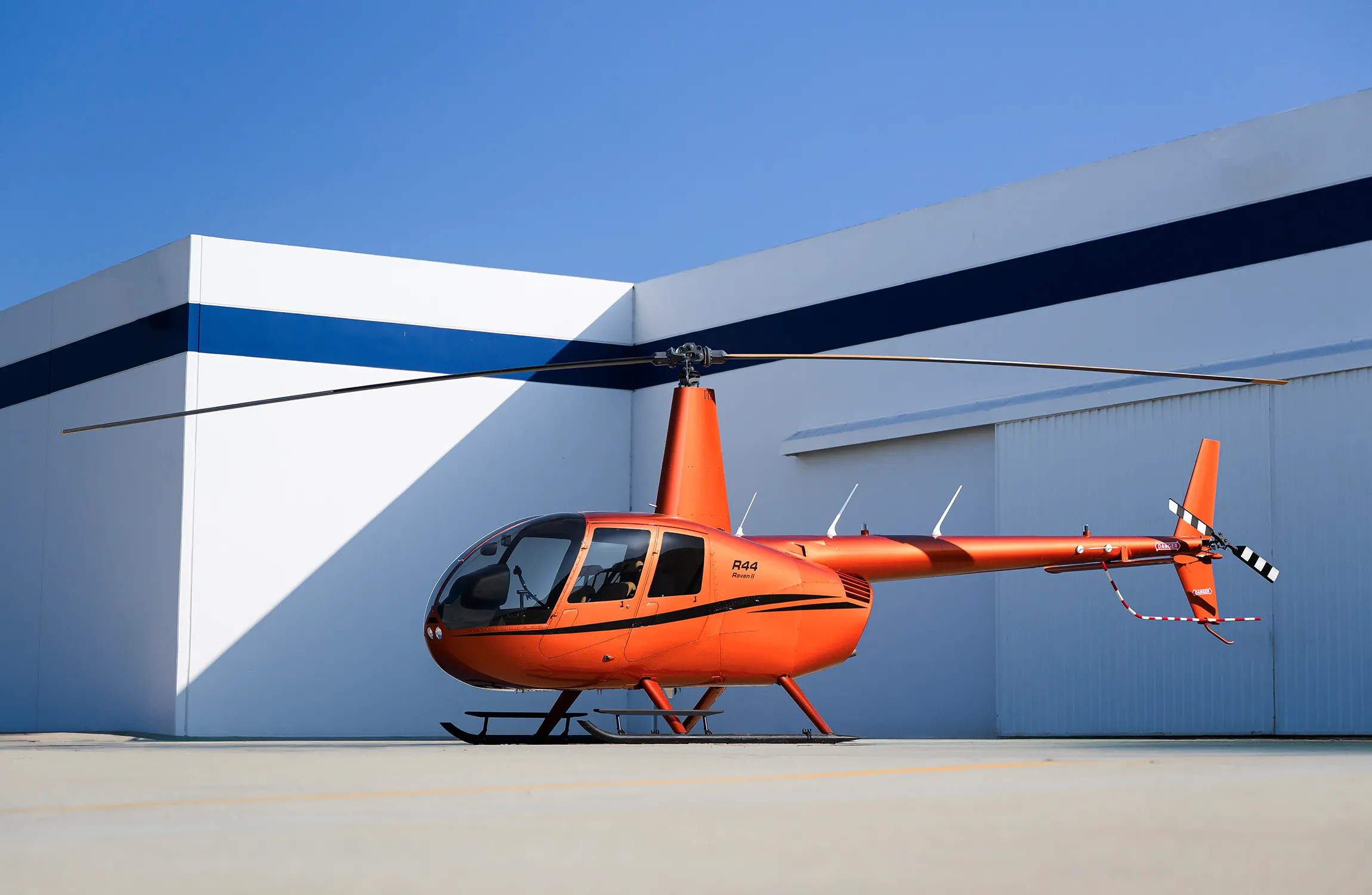 An orange helicopter parked in front of a hangar