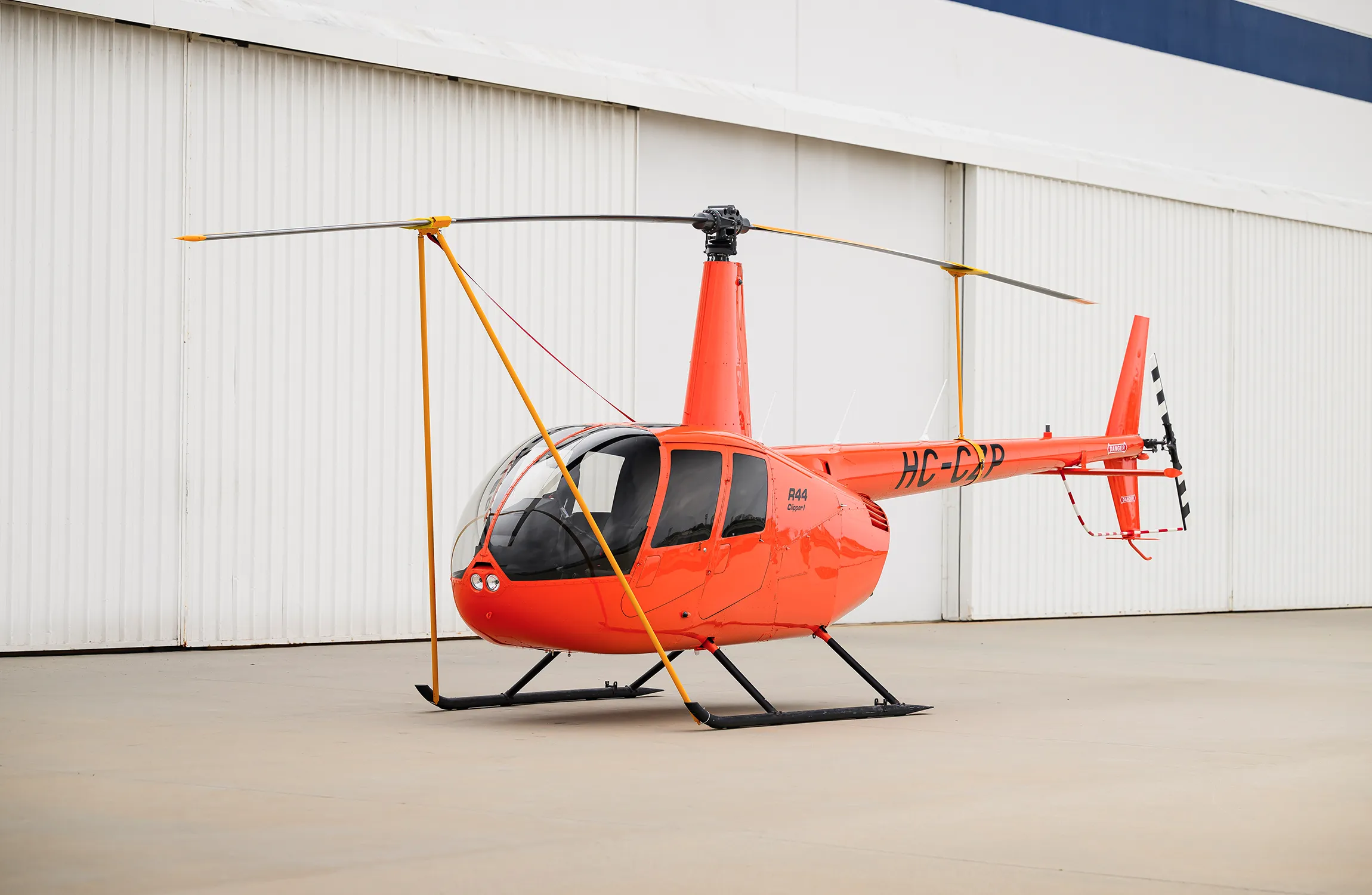 An orange helicopter parked in front of a hangar