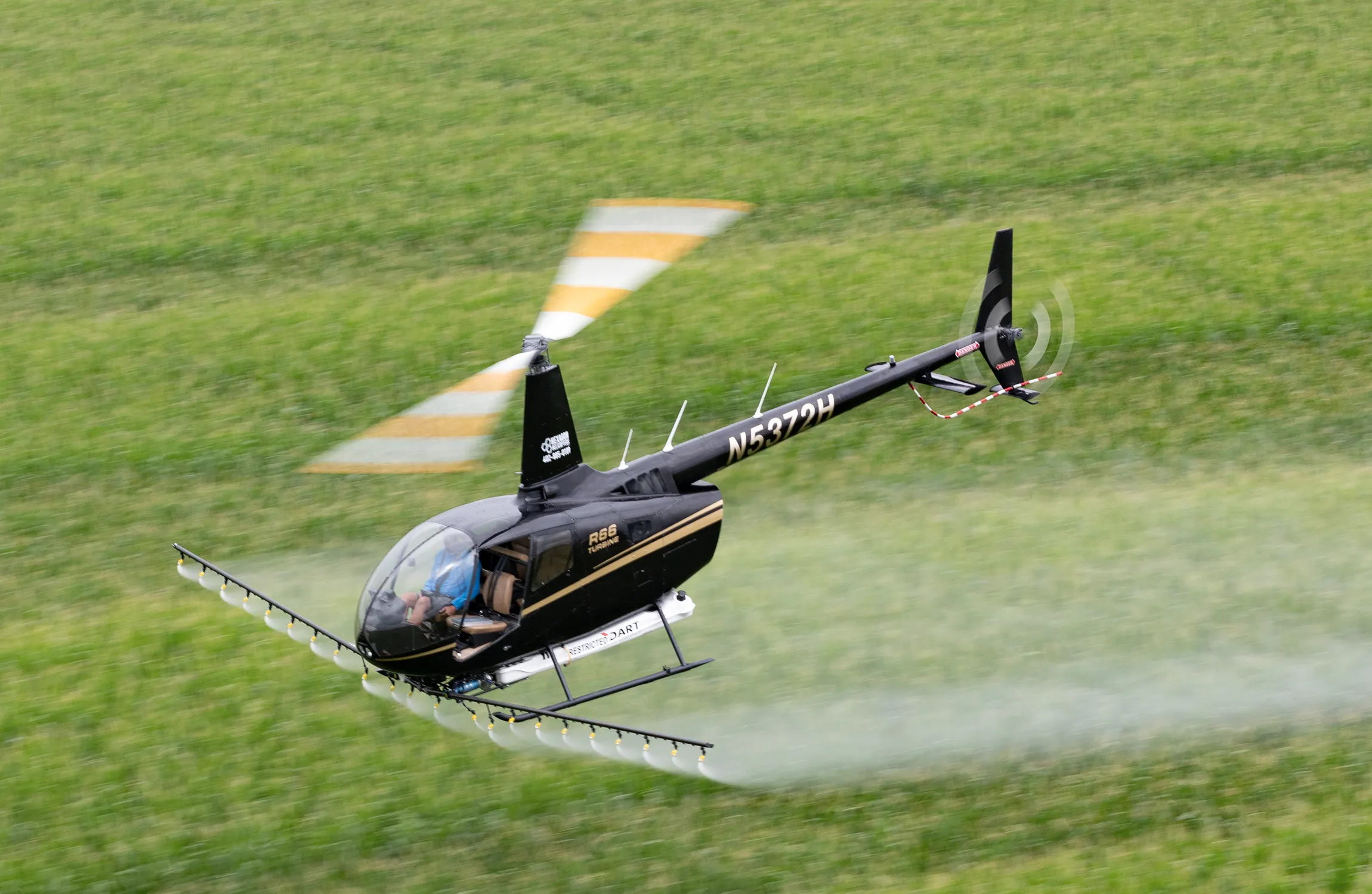 A black helicopter spraying a field