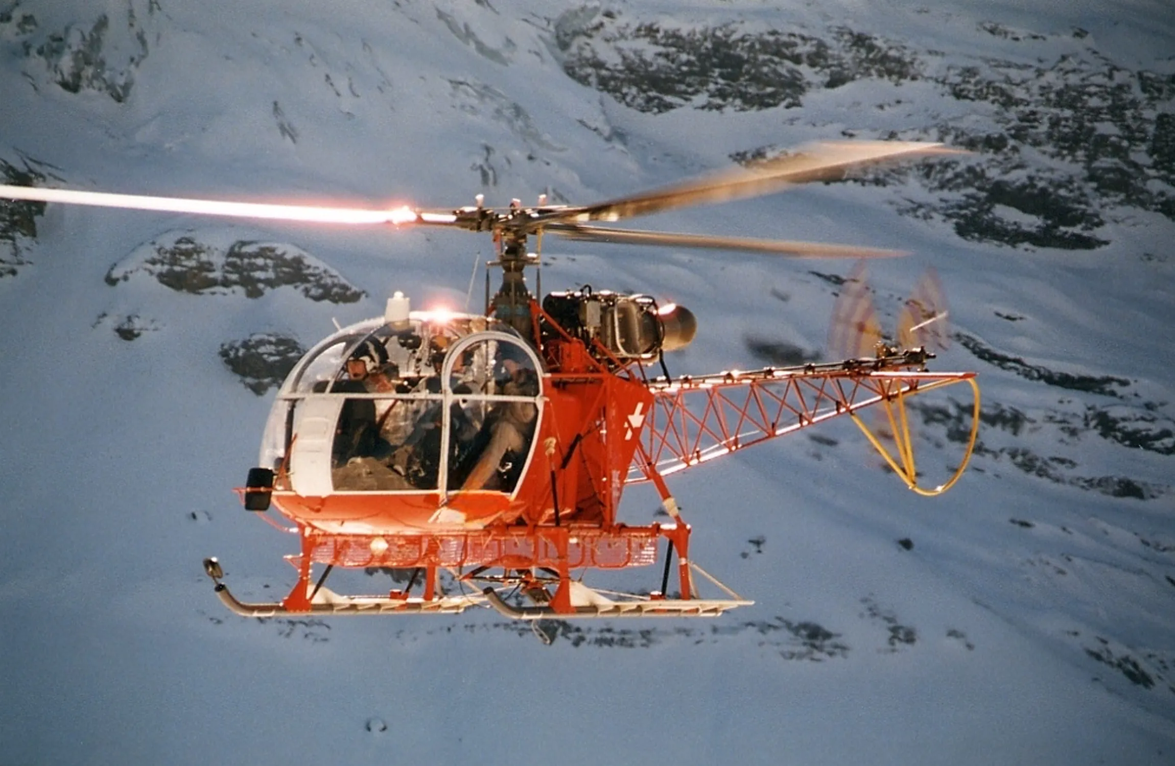 A red helicopter against a snowy mountain backdrop